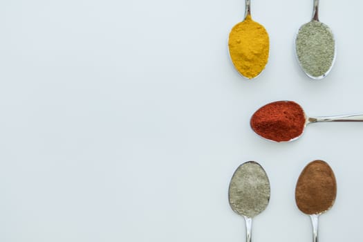 Various colorful spices arranged on spoons  with a white background