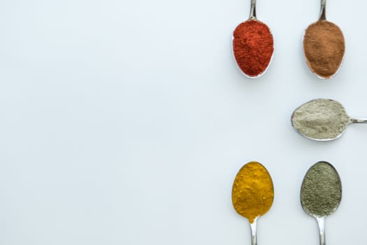 Various colorful spices arranged on spoons  with a white background