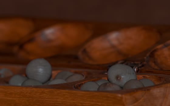 Closeup of a wooden mancala game with grey stones