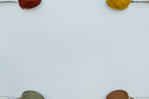 Various colorful spices arranged on spoons  with a white background