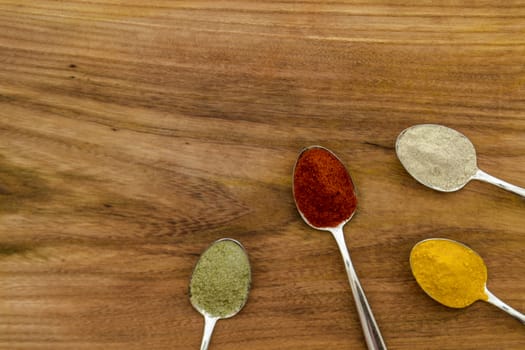 Various colorful spices arranged on spoons  with wooden background