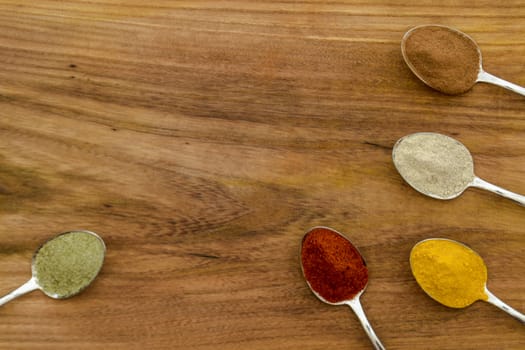 Various colorful spices arranged on spoons  with wooden background