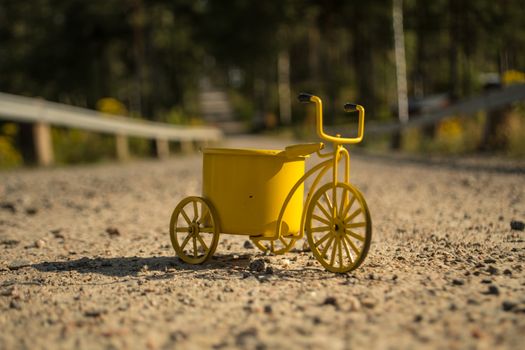 A yellow toy tricycle on a gravel road