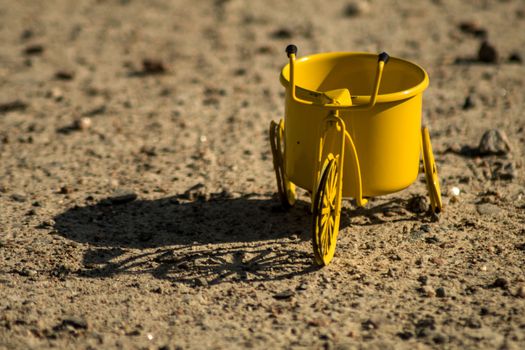 A yellow toy tricycle on a gravel road