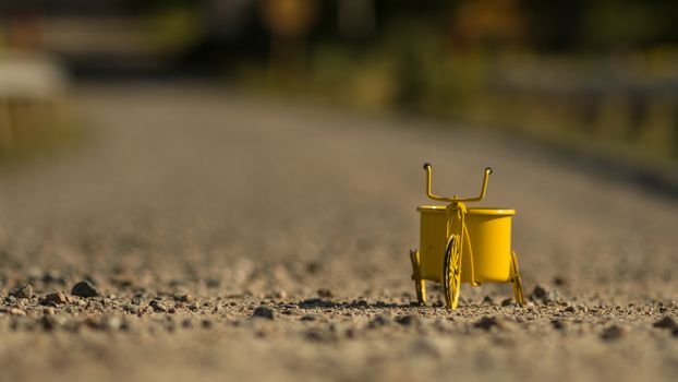 A yellow toy tricycle on a gravel road