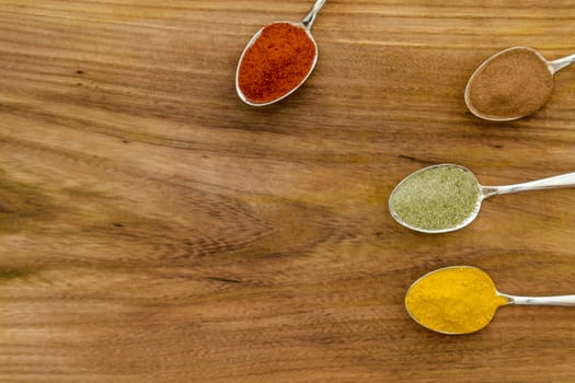 Various colorful spices arranged on spoons  with wooden background