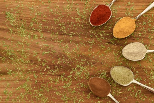Various colorful spices arranged on spoons  with wooden background