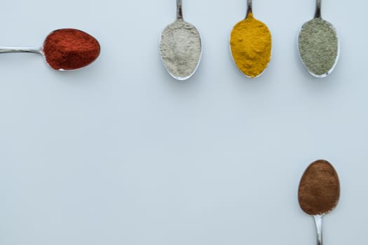 Various colorful spices arranged on spoons  with a white background