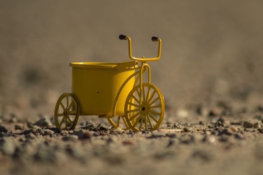 A yellow toy tricycle on a gravel road