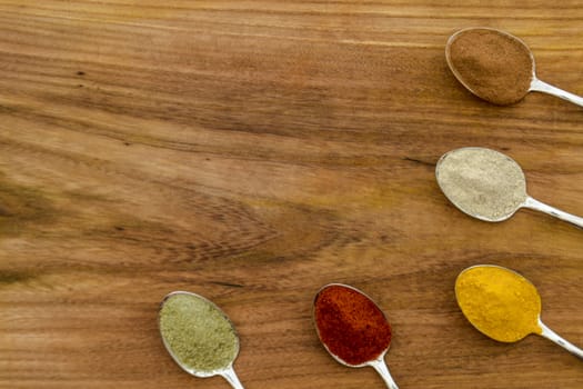 Various colorful spices arranged on spoons  with wooden background