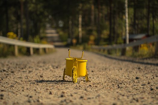 A yellow toy tricycle on a gravel road