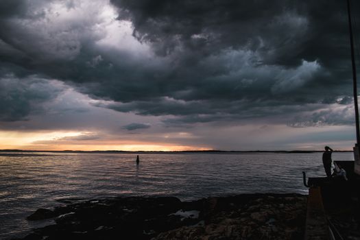 A person by the shore during stormy cloudscape and beautiful sunset
