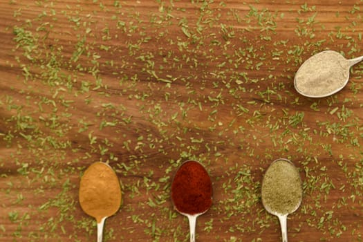 Various colorful spices arranged on spoons  with wooden background