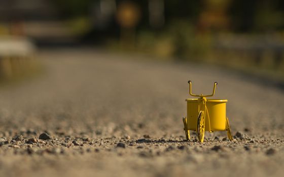 A yellow toy tricycle on a gravel road