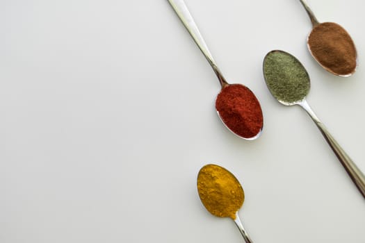 Various colorful spices arranged on spoons  with a white background