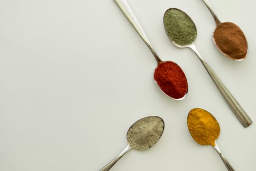 Various colorful spices arranged on spoons  with a white background