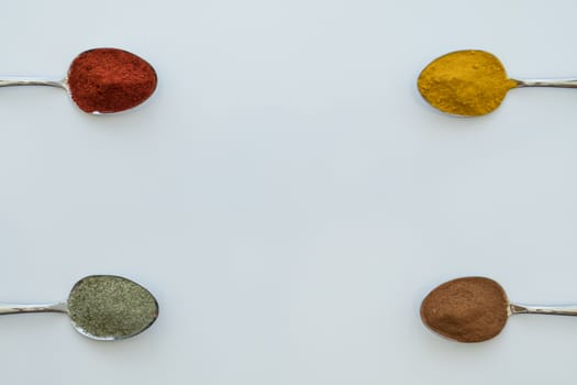 Various colorful spices arranged on spoons  with a white background