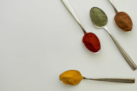 Various colorful spices arranged on spoons  with a white background