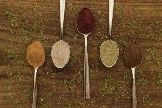 Various colorful spices arranged on spoons  with wooden background