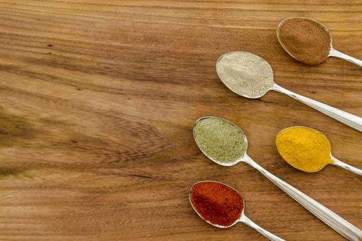 Various colorful spices arranged on spoons  with wooden background