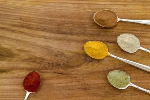 Various colorful spices arranged on spoons  with wooden background