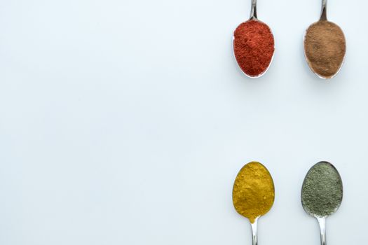 Various colorful spices arranged on spoons  with a white background