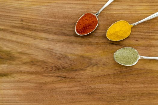 Various colorful spices arranged on spoons  with wooden background