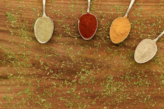 Various colorful spices arranged on spoons  with wooden background