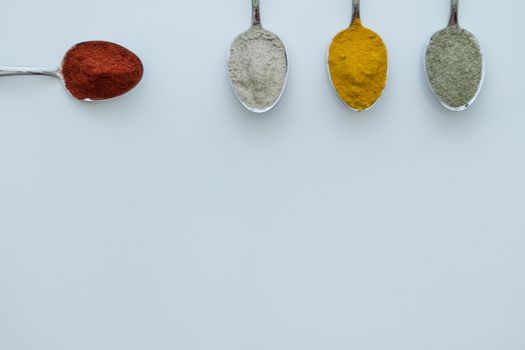 Various colorful spices arranged on spoons  with a white background