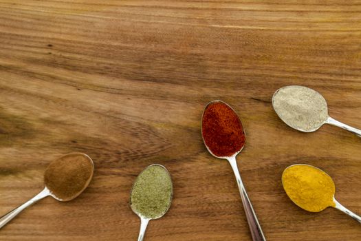 Various colorful spices arranged on spoons  with wooden background