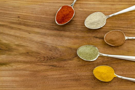 Various colorful spices arranged on spoons  with wooden background