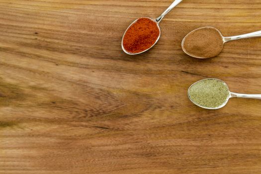 Various colorful spices arranged on spoons  with wooden background