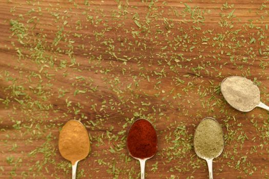 Various colorful spices arranged on spoons  with wooden background