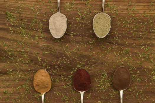 Various colorful spices arranged on spoons  with wooden background