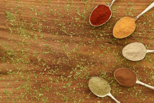 Various colorful spices arranged on spoons  with wooden background