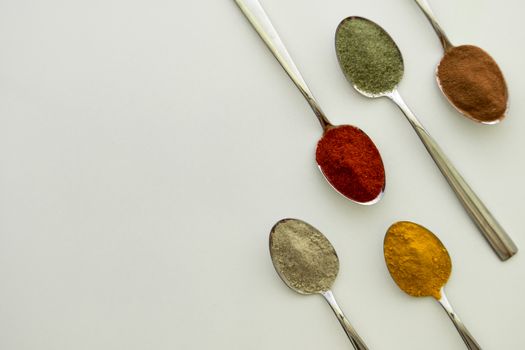 Various colorful spices arranged on spoons  with a white background