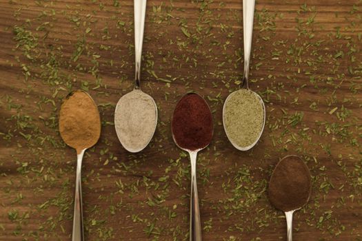 Various colorful spices arranged on spoons  with wooden background