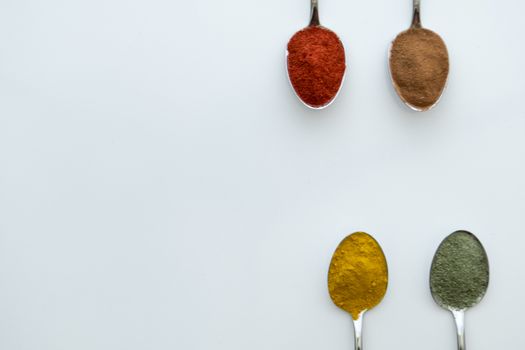 Various colorful spices arranged on spoons  with a white background