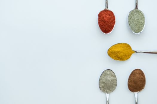 Various colorful spices arranged on spoons  with a white background