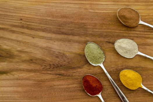 Various colorful spices arranged on spoons  with wooden background