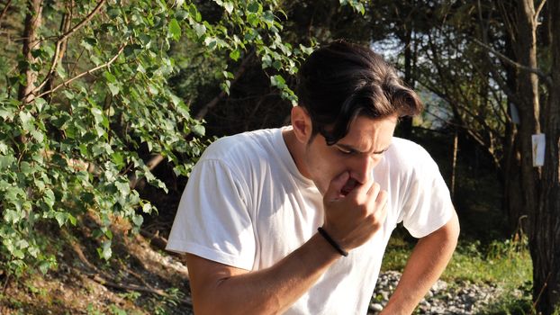 Young handsome man standing in nature, coughing, ill from flu or cold
