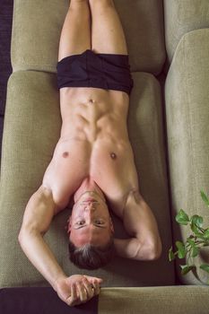 Shirtless, semi-naked fit young man resting on couch, seen from above
