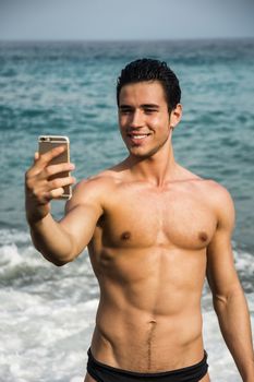 Side View of a Shirtless Young Man Taking Selfie Photos at the Beach While Standing Under the Sun.