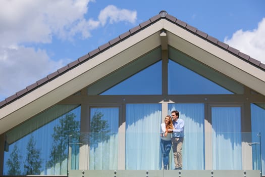 Happy couple standing on the balcony of their house and waving hands