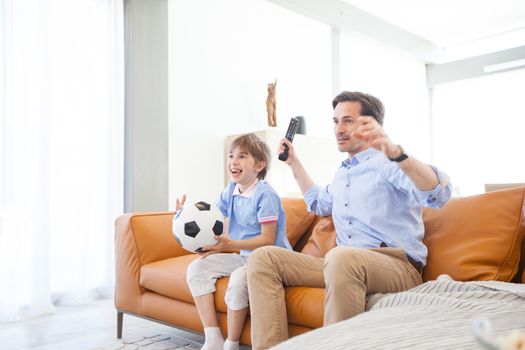 Portrait of happy boy watching soccer match with father on sofa at home