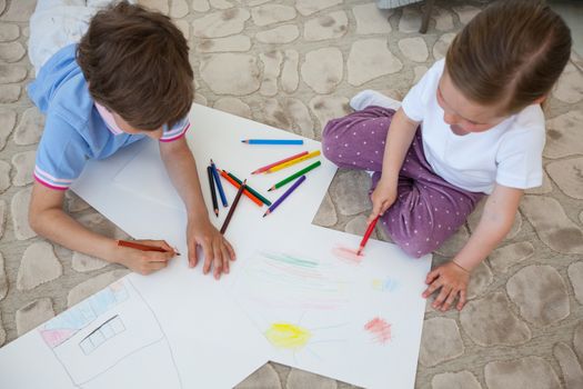 Little boy and girl drawing with color pencils on the floor playing together