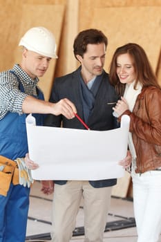 Worker shows house design plans to a young couple at construction site