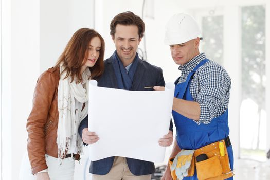 Worker shows house design plans to a young couple at construction site
