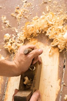 Closeup of woodworker's hands shaving with a plane in a joinery workshop