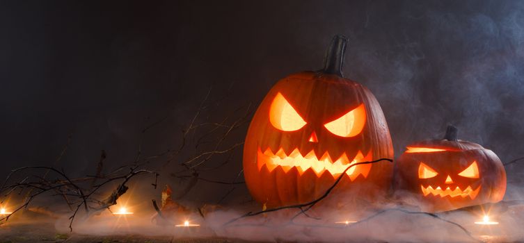 Halloween pumpkin heads jack o lantern and candles in fog on wooden background